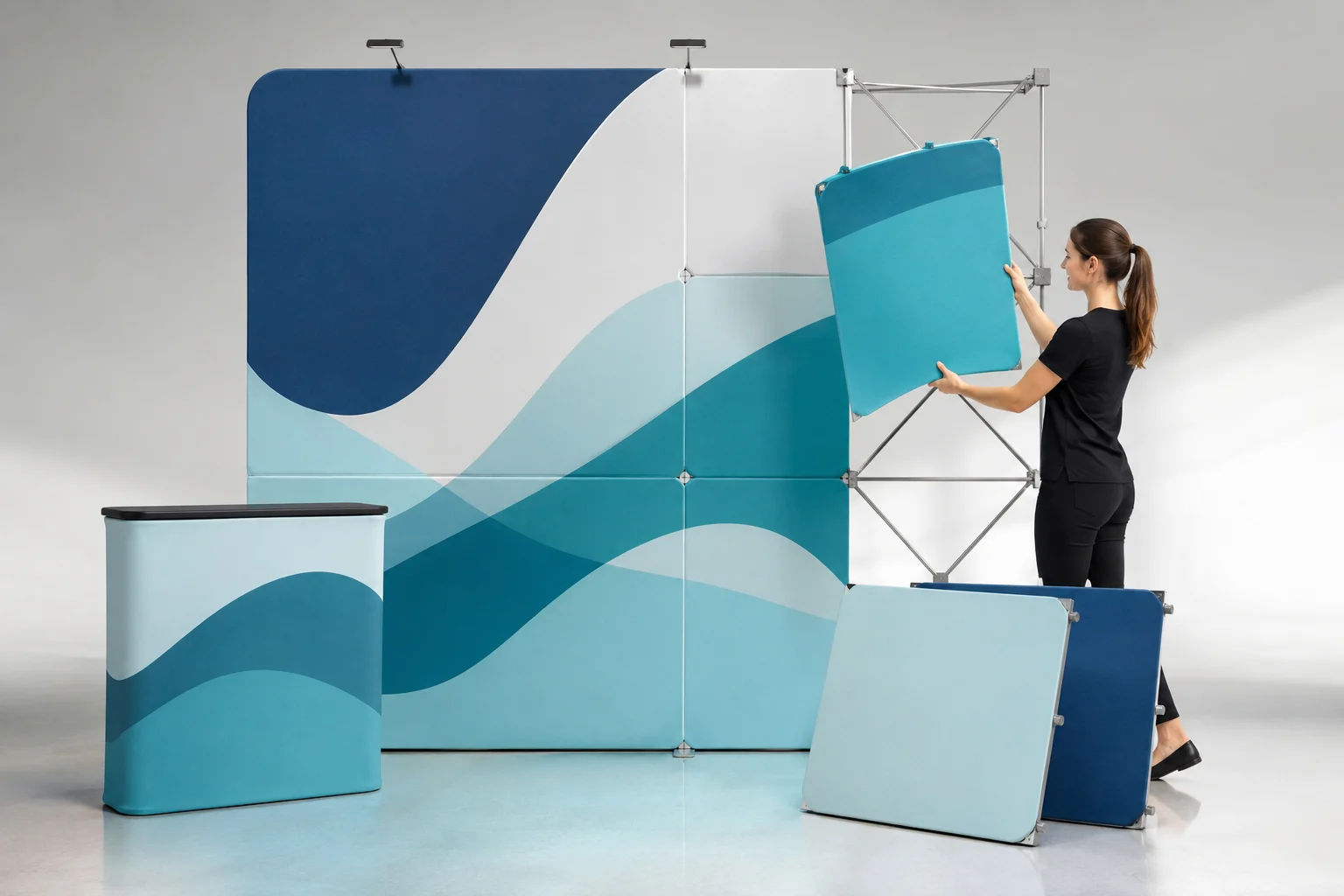Magnetic modular fabric display panels being assembled in a modern studio, featuring curved blue and teal fabric graphics, lightweight metal frames, and a portable counter.